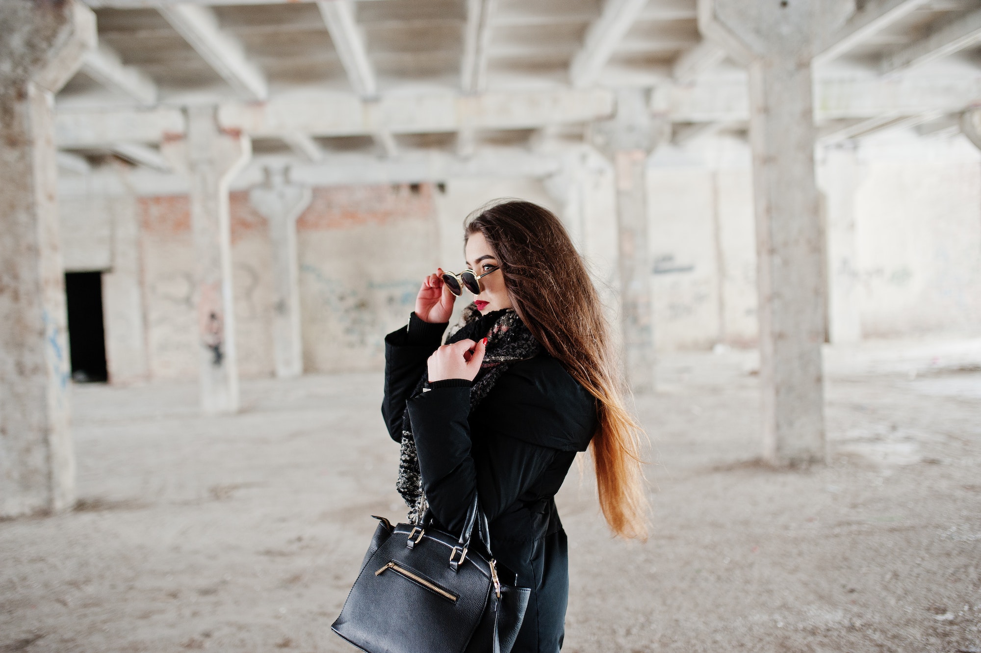 Brunette stylish casual girl in scarf and handbag against abandoned factory place.
